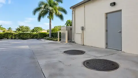 Two round grease interceptor covers in the paved rear service area of a small commercial building