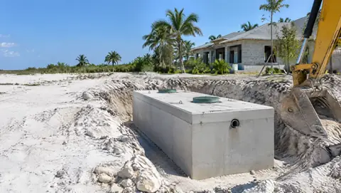 A new precast concrete septic tank set in a sandy limestone excavation next to an excavator bucket