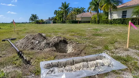 A soil test hole, a hand auger and soil cores of sand over limestone on a vacant lot with survey stakes